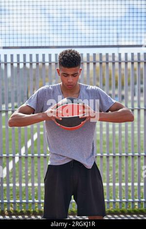 Porträt eines entschlossenen afroamerikanischen Sportlers in Sportbekleidung, der mit Basketball auf dem Sportplatz steht Stockfoto