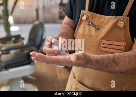 Von oben: Anonymer Friseur in Schürze mit spezieller Lotion zur Feuchtigkeitspflege bei der Arbeit im professionellen Salon Stockfoto