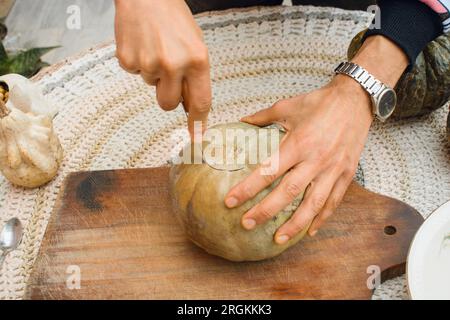 Draufsicht auf unbekannte männliche Hände zu Hause, Kürbis geschnitten, um halloween-Nacht auf Holzbrett zu dekorieren, Handwerkkonzept, Kopierraum. Stockfoto