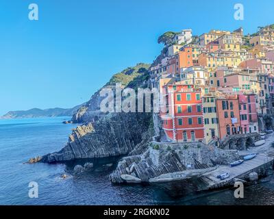 Panoramablick aus der Vogelperspektive auf die Stadt Riomaggiore mit vielen bunten Häusern und die Bucht mit kleinen Booten in Cinque Terre am Abend Stockfoto