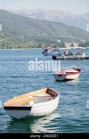 Ruderboote in einem See an sonnigen Tagen. Alte kleine hölzerne Fischerboote im Ohridsee mit grünen Bergen im Hintergrund. Stockfoto