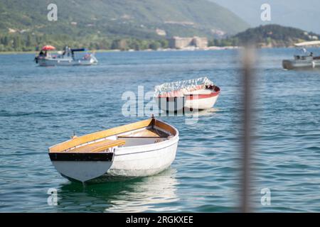 Ruderboote in einem See an sonnigen Tagen. Alte kleine hölzerne Fischerboote im Ohridsee mit grünen Bergen im Hintergrund. Stockfoto