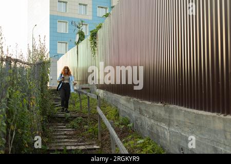 Das Mädchen geht die alte Treppe hoch. Durchgang zwischen Zäunen. Dorf- und Stadtgrenze. Mädchen läuft in einer unbekannten Gegend. Stockfoto