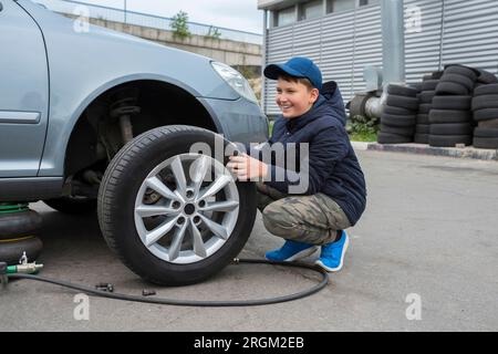 Der Junge hilft beim Autoservice. Wenn die Räder am Fahrzeug ausgetauscht werden, hält der Wagenheber die Karosserie in angehobener Position Stockfoto