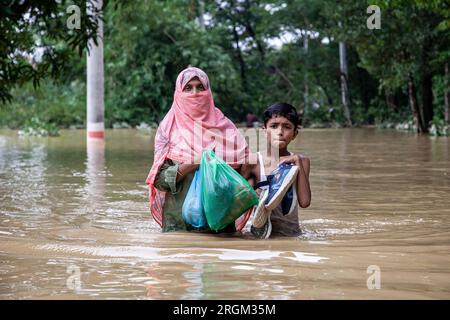 Chittagong, Bangladesch. 10. August 2023. Fußgänger laufen durch überflutete Straßen im Wasser bis zur Brust und Taille in Satkania Upazila im Süden von Chittagong. Das Leben der Menschen wurde durch anhaltende Regenfälle an fünf aufeinanderfolgenden Tagen schwer gestört. Etwa 242 km südöstlich von Chittagong, Bangladeschs Hafenstadt, wurden tiefliegende Gebiete überflutet und der Straßenverkehr mit den höchsten Niederschlägen gestört. Stockfoto