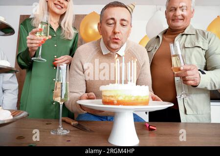 Ein reifer Mann mit Freunden, der sich auf der Geburtstagsparty in der Küche wünscht Stockfoto