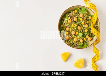 Schüssel mit frischem Salat und Maßband auf weißem Hintergrund. Diätkonzept Stockfoto