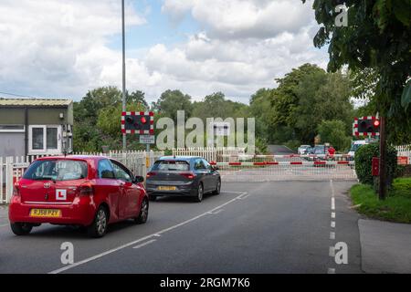 Der Bahnübergang in Kintbury, Berkshire, England, Großbritannien, mit Autos und einem Radfahrer, der darauf wartet, dass sich die Tore öffnen Stockfoto