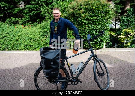 Rotterdam, Südholland, Niederlande, 4. Juli 2023 - 44 Yo man mit Trekkingrad vor einem grünen Hintergrund Stockfoto