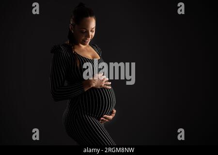 Lächelnde Schwangere in gestreiftem Kleid mit schwarzem Hintergrund Stockfoto