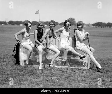 Frauen in Badeanzügen und mit Golfschlägern auf einem Golfplatz, die auf einem Eisblock sitzen. 1926 Stockfoto