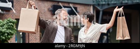 Banner, aufgeregtes und älteres Paar mit Einkaufstaschen, Stadtleben, glücklicher Mann und glückliche Frau Stockfoto
