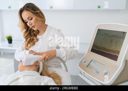 Porträt einer kaukasischen Kosmetikerin mit Ausrüstung für Ultraschallhebungsverfahren bei blonder Mandantin. Stockfoto