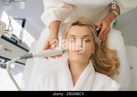 Detailansicht von oben abgeschnittene Aufnahme einer nicht erkennbaren Ärztin mit nichtinvasiver RF-Gesichtsheberung an einer jungen Frau zur Verjüngung Stockfoto