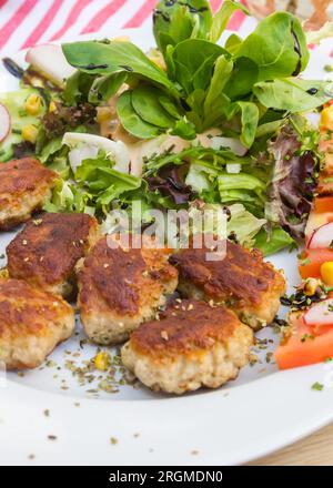 Traditionelle deutsche kleine Fleischbällchen (Frikadelle), serviert mit Salat und Tomaten auf einem weißen Teller Stockfoto