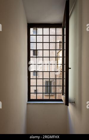 Ein schmaler Flur in einem Gebäude mit einem schwarzen Metallgitterfenster, in das Licht eindringt Stockfoto