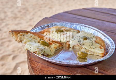 Leckere Pizzaschneiden am Strand, mit Mozzarella und Oliven auf einem Holztisch im Sommer Stockfoto