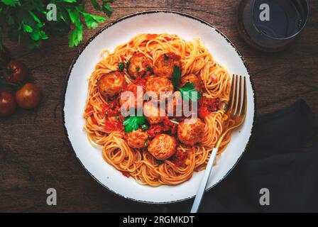 Spaghetti-Pasta mit Schweinefleisch und Rindfleischklößchen in Tomatensoße mit Petersilie im Teller, Holztisch im Hintergrund, Draufsicht Stockfoto