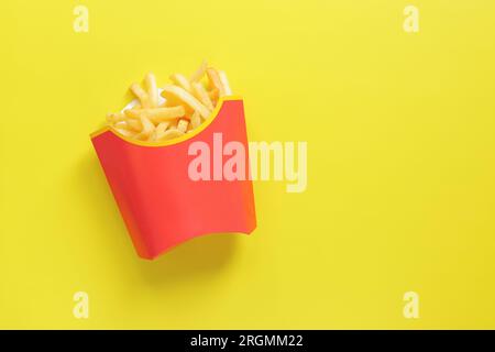 Pommes frites auf gelbem Hintergrund, Draufsicht. Kartoffeln in Papierverpackungen Stockfoto