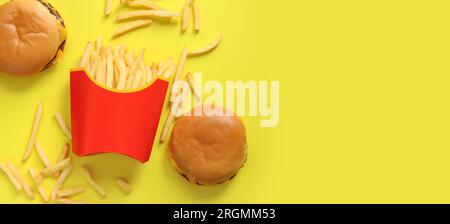 Pommes frites in Papierverpackung und Burger auf gelbem Hintergrund, Draufsicht. Fastfood. Platz kopieren, für Text platzieren Stockfoto