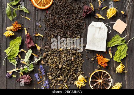 Zusammensetzung von trockenem schwarzen und grünen Tee, Teebeutel, getrockneten Zitrusscheiben und trockenen Hibiskusblumen auf dunklem Holzhintergrund von oben. Verschiedene Arten von Stockfoto