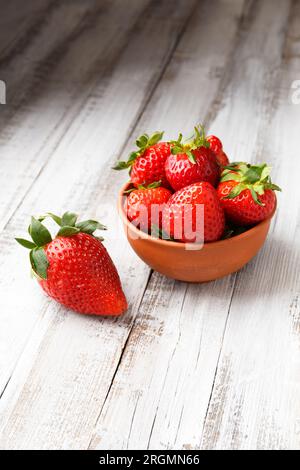 Reife, saftige, große organische Erdbeeren in einer Tonkeramikschüssel auf Holzhintergrund. Stockfoto