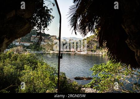 Blick aus einem Fenster in die Landschaft von Taormina, Sizilien in Italien. Von Bäumen bedeckte Hügel und Strand Stockfoto