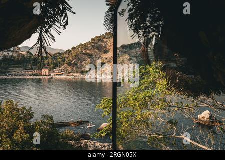 Blick aus einem Fenster in die Landschaft von Taormina, Sizilien in Italien. Von Bäumen bedeckte Hügel und Strand Stockfoto