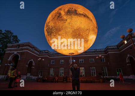 London, Großbritannien. 10. August 2023. Mars: War & Peace von Luke Jerram. Eine 7 Meter breite rotierende Nachbildung des mars von Luke Jerram, die derzeit am Jubilee Square in Kensington ausgestellt wird. Die monumentale, hängende, intern beleuchtete Skulptur wurde unter Verwendung von NASA-Bildern mit 120dpi detaillierten Bildern der Marsoberfläche gebaut. Etwa eine Million Mal kleiner als der eigentliche Planet, stellt jeder Zentimeter der kugelförmigen Skulptur 10 Kilometer der Marsoberfläche dar. Kredit: Guy Corbishley/Alamy Live News Stockfoto