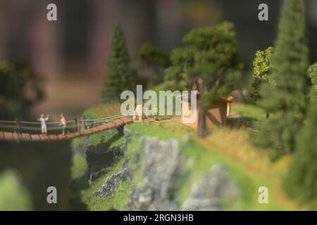 Spielzeugmodell des Parks. Leute auf der Brücke. Bergtouristen im Sommer. Figuren von Menschen aus Plastik. Miniatur unter Glas. Layout des Bereichs. Stockfoto