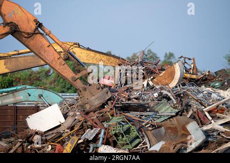 Magnet des Hydraulikbaggers hebt Stahlschrott aus dem Recyclingmaterialhaufen auf dem Schrottplatz in der Recyclingfabrik. Bagger mit Elektro- und Magnetsauger Stockfoto