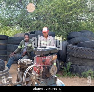 afroamerikanische Straßenräuber hinter einem Kompressor, Reifenreparatur und -Aufpumpen für einen Lebensunterhalt, Arbeiterteam in Arbeitskleidung Stockfoto