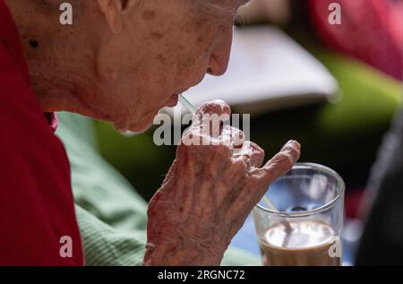 Berlin, Deutschland. 31. Juli 2023. Brigitte Richter, eine 97-jährige Seniorin in Pflegebedürftigkeit, trinkt Kaffee aus einem Glas, das von einer Krankenschwester mit einem Strohhalm in ihr Zimmer gebracht wurde. Kredit: Monika Skolimowska/dpa/Alamy Live News Stockfoto