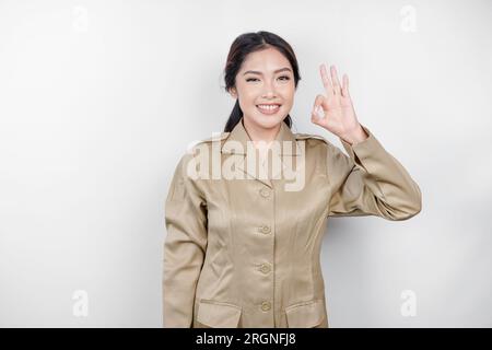 Eine junge asiatische Frau in brauner Khaki-Uniform, die mit ihren Fingern ein OK-Zeichen zeigt. Indonesischer Regierungsangestellter. Stockfoto