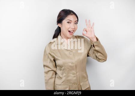 Eine junge asiatische Frau in brauner Khaki-Uniform, die mit ihren Fingern ein OK-Zeichen zeigt. Indonesischer Regierungsangestellter. Stockfoto