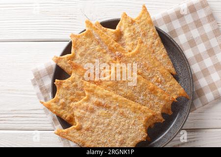 Französische süße Oreillette Karneval-Fritters, die auf dem Teller auf dem Holztisch zusammengelegt werden. Horizontale Draufsicht von oben Stockfoto