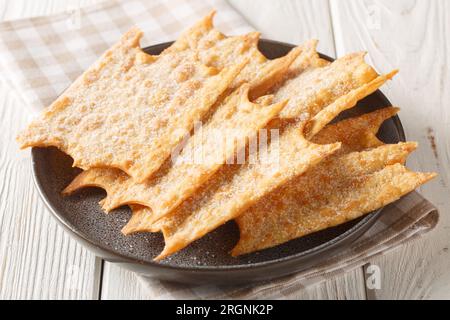 Französische süße Oreillette Karneval-Fritters, die auf dem Teller auf dem Holztisch zusammengelegt werden. Horizontal Stockfoto