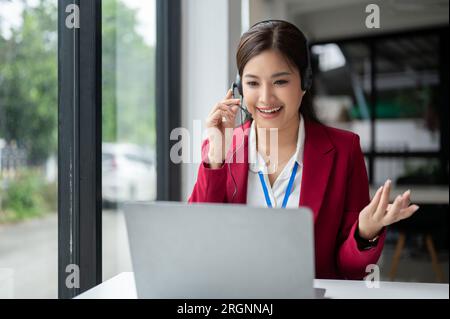 Eine zuversichtliche und zufriedene asiatische Kundendienstmitarbeiterin oder Callcenter-Agentin spricht und berät einen Kunden telefonisch oder Stockfoto