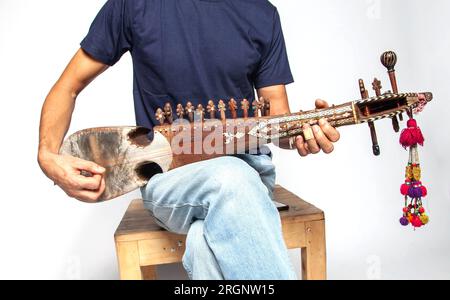 Ein Mann, der ein östliches Volksinstrument aus Nordpakistan spielt, isoliert auf weißem Hintergrund. Stockfoto