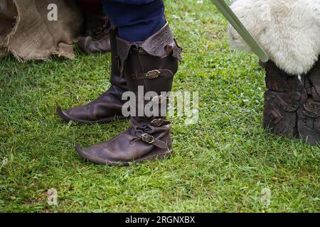 Beine eines Mannes in mittelalterlichen Lederstiefeln auf dem Gras Stockfoto