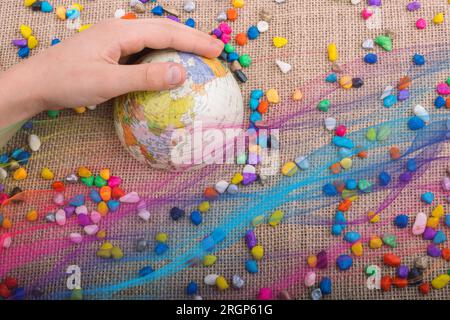 Modellkugel unter der Hand inmitten von kleinen bunten Kieselsteinen Stockfoto