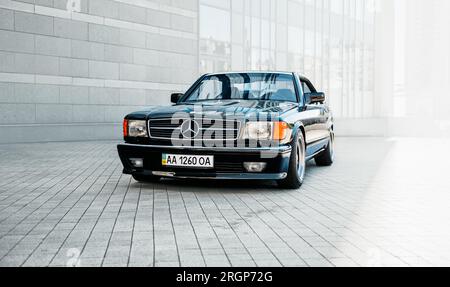 Der klassische schwarze Mercedes-Benz W126 parkt an einem sonnigen Tag in der Nähe eines gewöhnlichen Bürogebäudes. Dreiviertelansicht des Luxus-Coupés aus dem 1980er Stockfoto