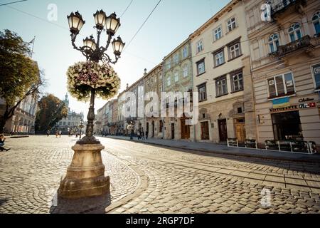 Vormittag in der Altstadt von Lemberg. Der halb leere Marktplatz und der Lampenpfahl in Middletown sind mit Sonnenlicht gefüllt, das aus dem Hintergrund kommt. Stockfoto