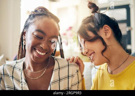 Glücklich, lachend und Freunde tratschen, reden und verbinden sich mit Witzen, Humor und Geschichten in ihrem Zuhause. Lächeln, lustig und Frauen mit Abwechslung im Wohnzimmer Stockfoto