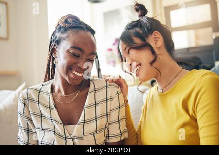 Fröhliche, lustige und Freunde tratschen, reden und verbinden sich mit Witzen, Humor und Geschichten in ihrem Zuhause. Lächeln, Lachen und Frauen mit Vielfalt im Wohnzimmer Stockfoto