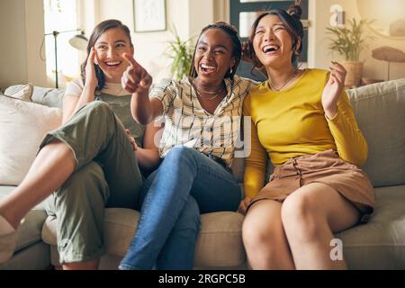 Glücklich, Freunde und Frauen, die auf dem Sofa fernsehen, lachen, sich verbinden und sich am Wochenende in ihrem Zuhause entspannen. Fernsehen, Film und Menschen mit Vielfalt in Stockfoto