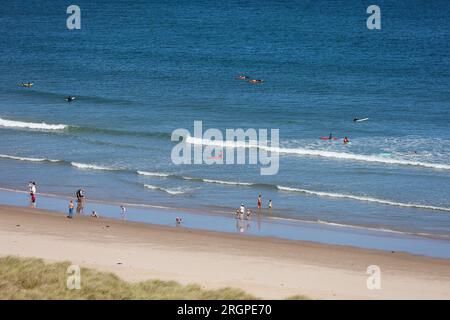 Bamburgh, Northumberland, Großbritannien. 11. August 2023. UK Weather: Ein heller und sonniger Tag am Strand von Bamburgh, an dem Besucher und Surfer die Sonne genießen. Bildnachweis: PAL News/Alamy Live News Stockfoto