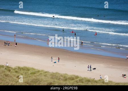 Bamburgh, Northumberland, Großbritannien. 11. August 2023. UK Weather: Ein heller und sonniger Tag am Strand von Bamburgh, an dem Besucher und Surfer die Sonne genießen. Bildnachweis: PAL News/Alamy Live News Stockfoto