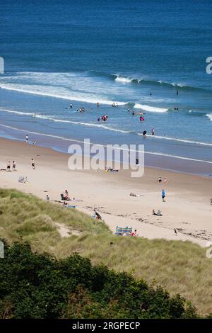 Bamburgh, Northumberland, Großbritannien. 11. August 2023. UK Weather: Ein heller und sonniger Tag am Strand von Bamburgh, an dem Besucher und Surfer die Sonne genießen. Bildnachweis: PAL News/Alamy Live News Stockfoto