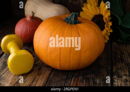 Herbstliche Kürbisse, Hantel, Sonnenblumen. Gesunde Fitness Herbstkomposition für Halloween oder Thanksgiving. Fitness-Training und Sporttrainingskonzept. Stockfoto